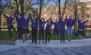 10 youth jumping in the air with their hands up. All are wearing purple shirts which represent their CWSF Ambassador leadership position.