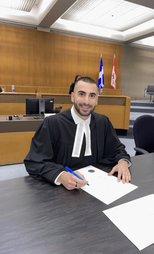 Skilled young lawyer in formal gown reviewing legal documents in a modern courtroom setting with Canadian flags in the background.