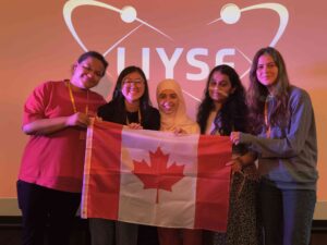Diverse group of young women holding a Canadian flag at the London International Youth Science Forum, promoting STEM education and international youth participation.
