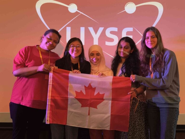Diverse group of young women holding a Canadian flag at the London International Youth Science Forum, promoting STEM education and international youth participation.