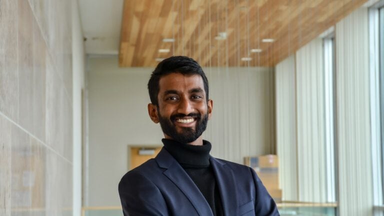 Young professional man smiling, standing indoors with modern architecture, natural light, and wooden ceiling, representing youth STEM engagement at Youth Science Canada.
