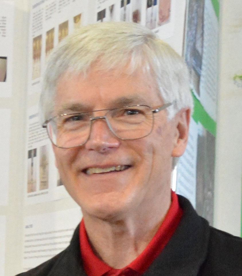 Portrait of Chuck Buckley, a senior man with glasses and white hair, smiling at a science event, representing Youth Science Canada and inspiring youth engagement in science.