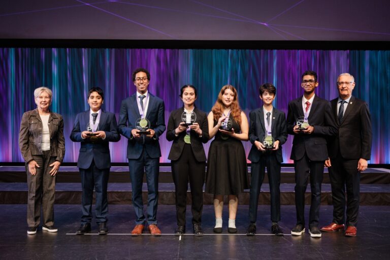 A young group of diverse students and adults on stage at Youth Science Canada awards ceremony, holding trophies and celebrating achievements in science and innovation.